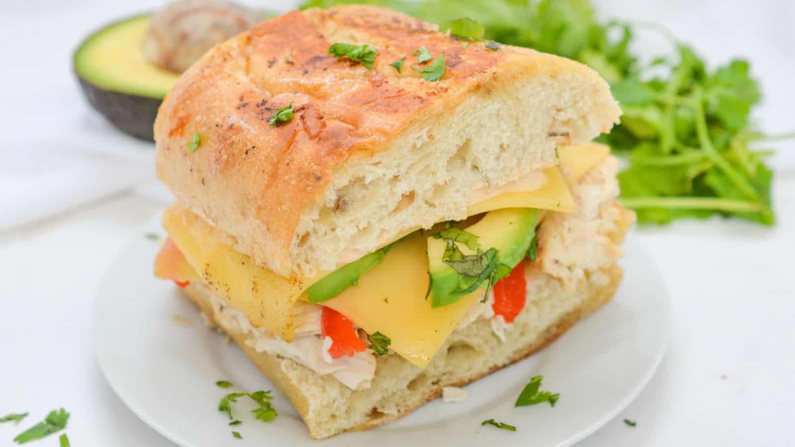 A sandwich with avocado, chicken and cheese on a plate.