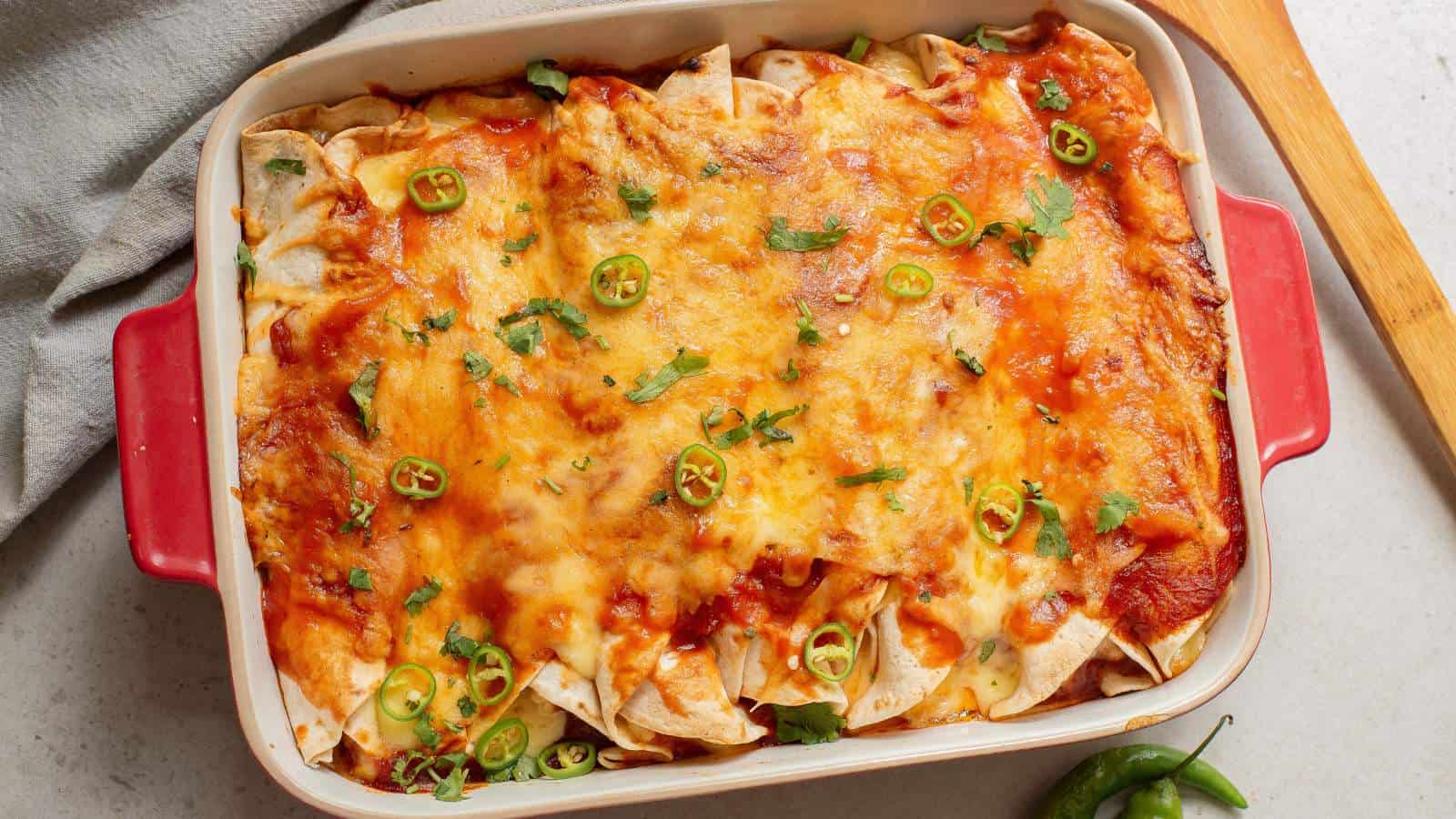 Chicken enchiladas in a casserole dish with diced jalapeno and green onion.