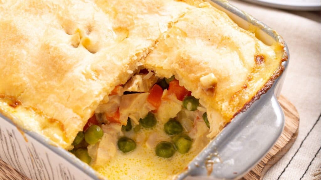A freshly baked chicken pot pie with a golden crust, portions of which have been served, revealing its creamy filling with vegetables.