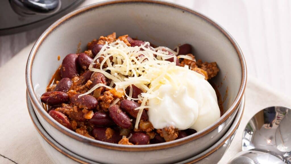 A bowl of chili topped with shredded cheese and a dollop of sour cream.