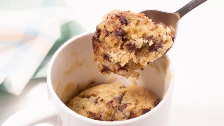 A spoon lifting a bite from a chocolate chip mug cake in a white mug.