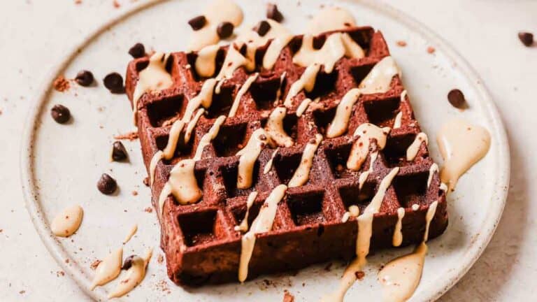 Chocolate waffle topped with peanut butter drizzle and chocolate chips, served on a ceramic plate.