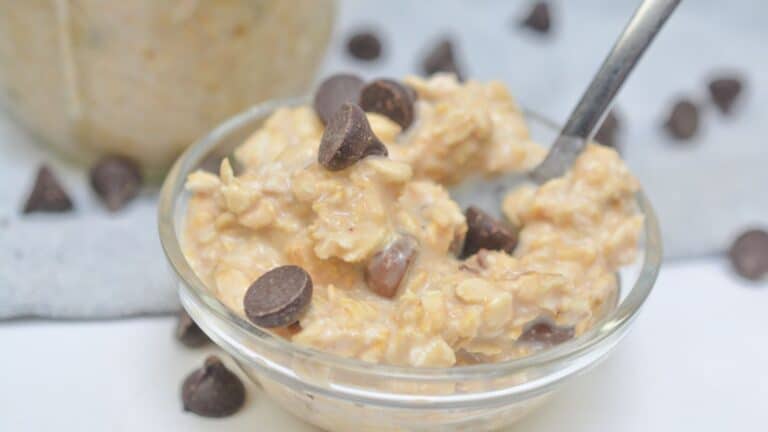 A bowl of oatmeal with chocolate chips on top, accompanied by a spoon, set on a white surface with scattered chocolate chips around.