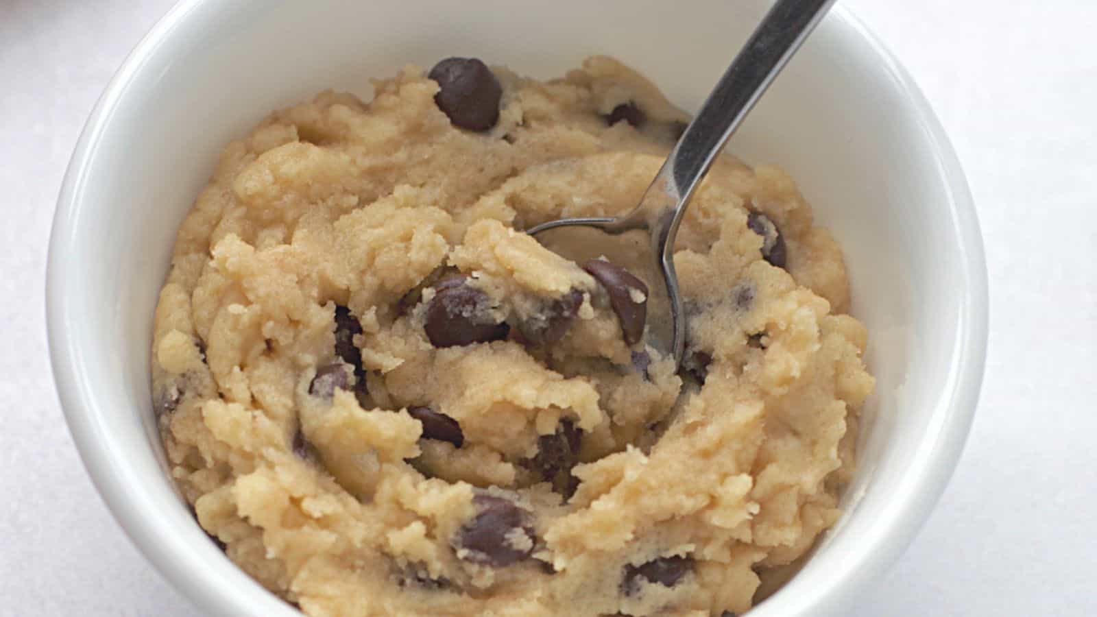 Edible chocolate chip cookie dough in white bowl with spoon.