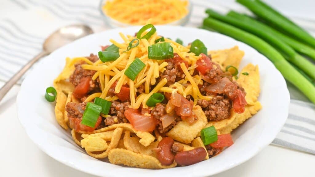 A plate of Fritos topped with ground beef, cheese, tomatoes, beans, and green onions.