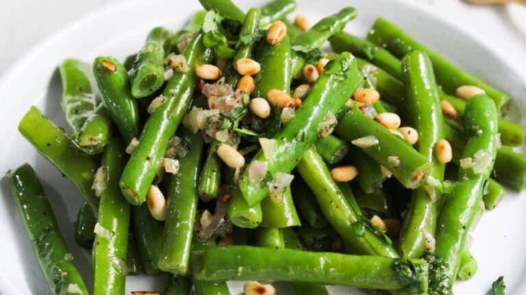 A dish of green beans tossed with herbs and pine nuts.