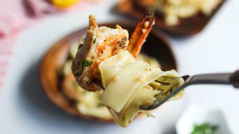 Fork lifting a shrimp and pasta dish, with more food in the background.