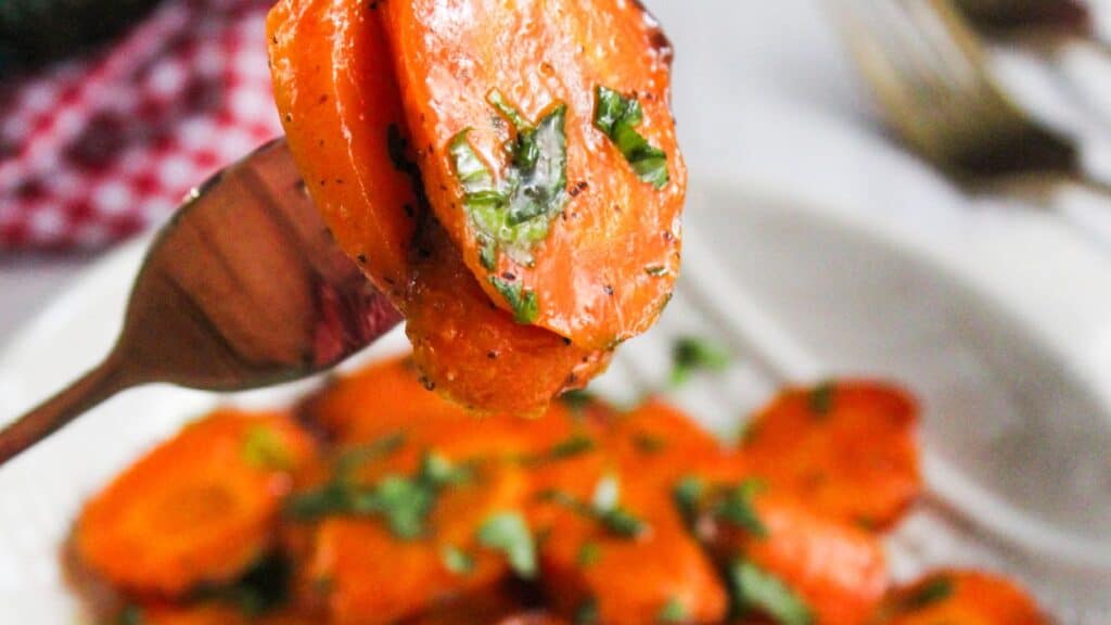 Honey-glazed carrot slice on a fork, with chopped parsley garnish.
