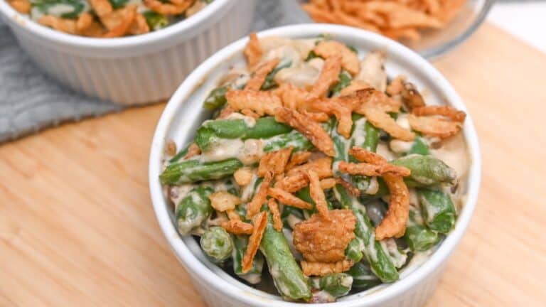 A ramekin of green bean casserole topped with crispy fried onions, served on a wooden table.