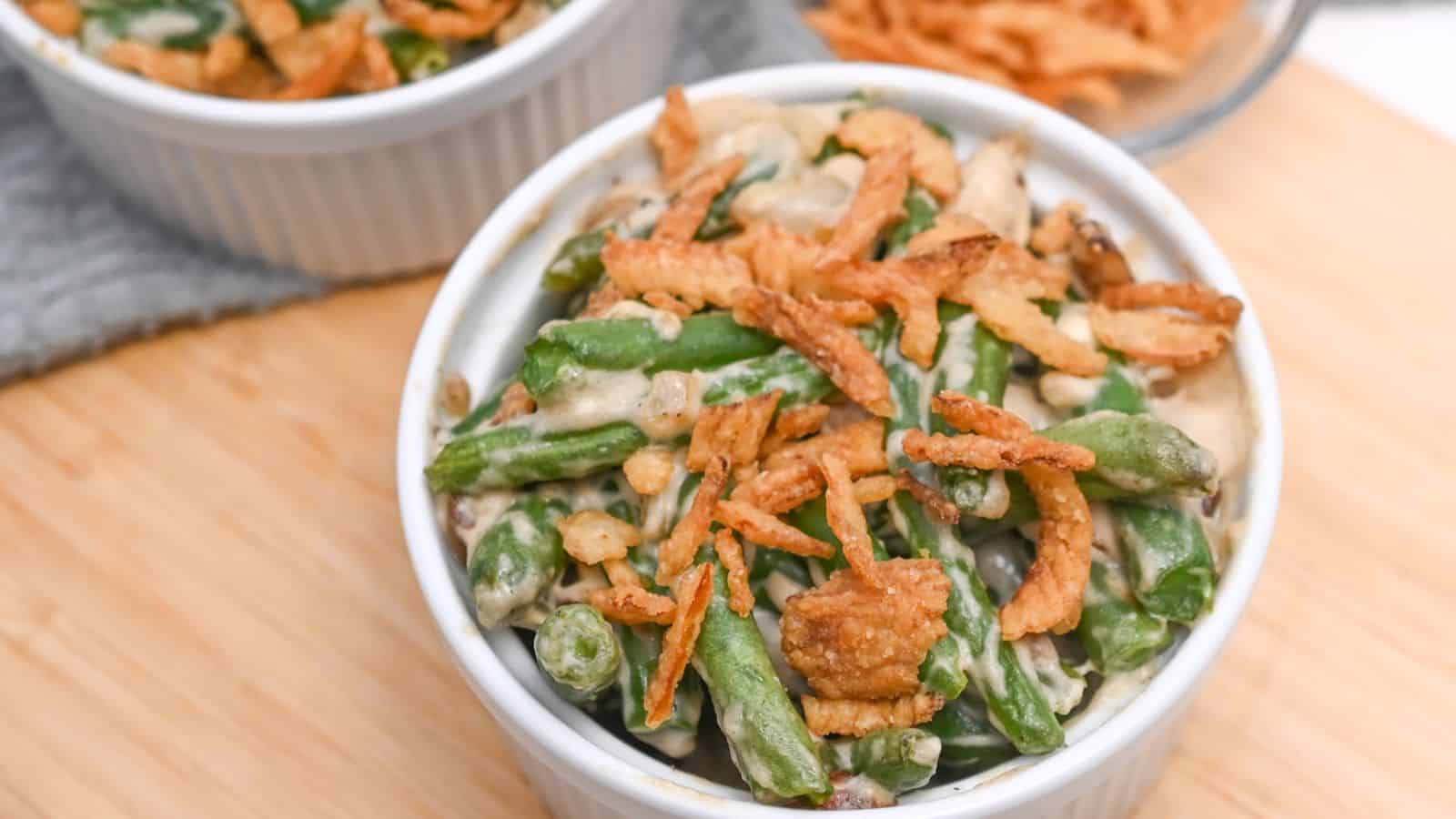 A ramekin of green bean casserole topped with crispy fried onions, served on a wooden table.