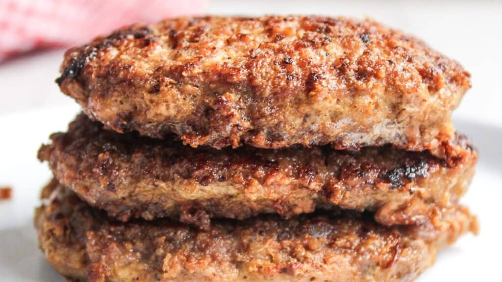 Close-up of grilled pork burger patties stacked on a white plate.