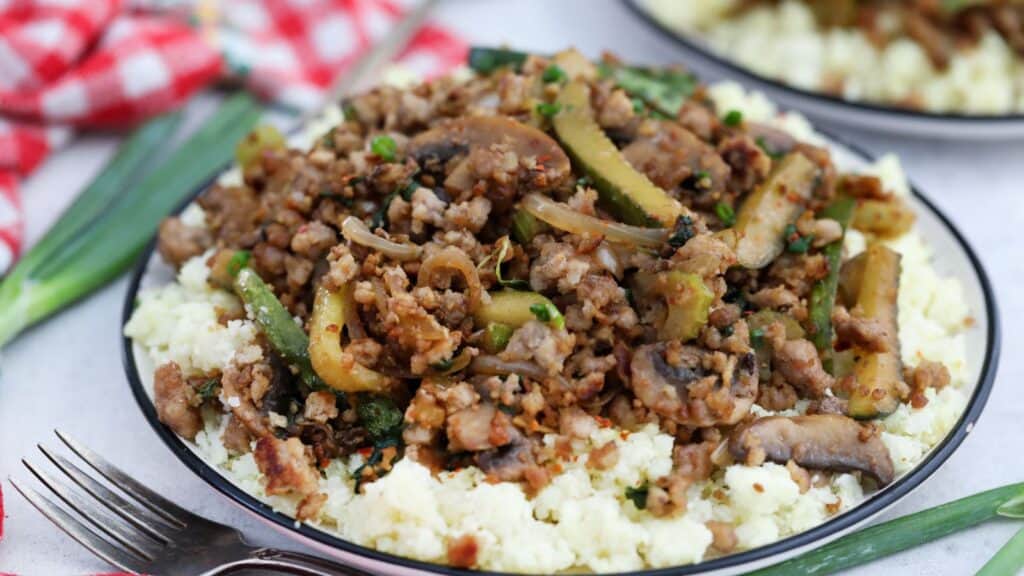 A plate with ground pork and vegetables on top of cauliflower rice.