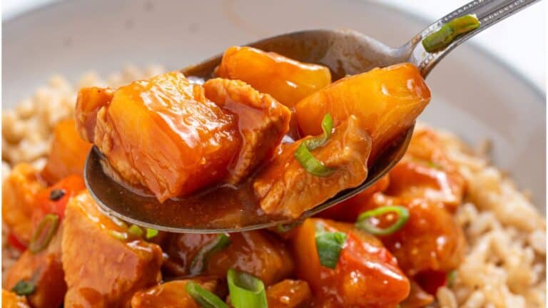 Close-up of a spoon scooping up Hawaiian chicken with pineapple and green onions, served over rice.