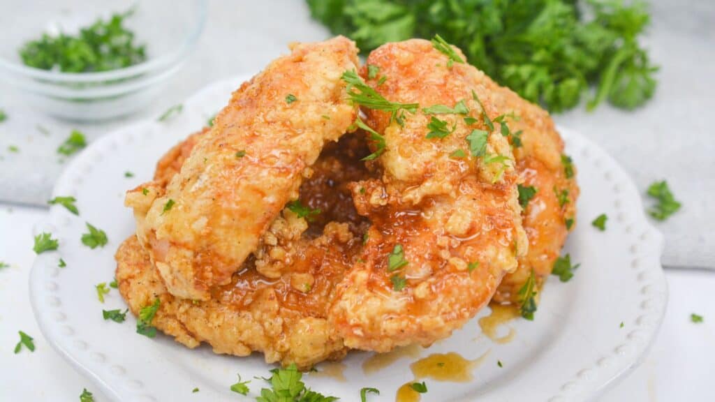 Fried chicken with a crispy coating garnished with parsley on a white plate.