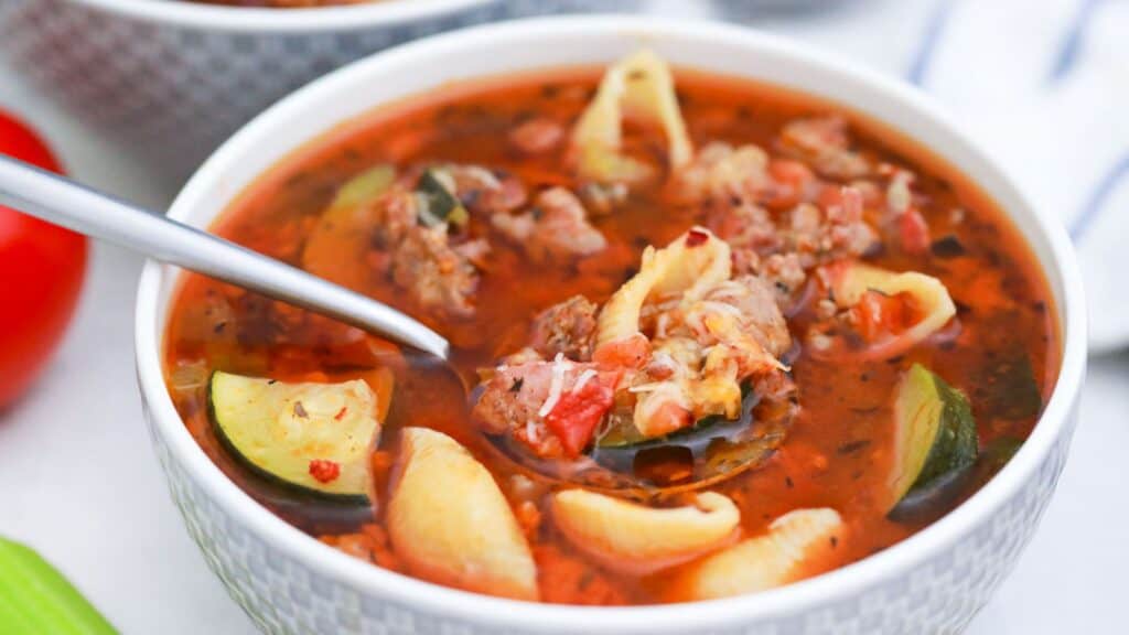 A bowl of hearty vegetable and meat soup with a spoon.