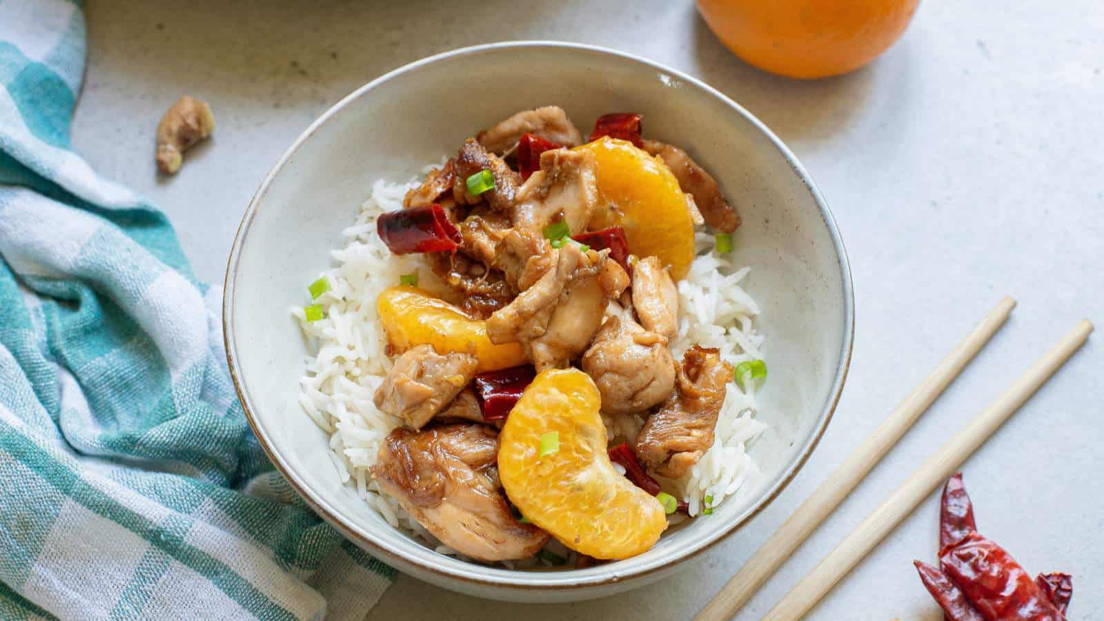 Mandarin chicken over rice in a white bowl with chopsticks.
