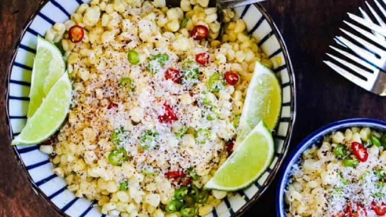 A bowl of seasoned corn salad with lime wedges on the side.