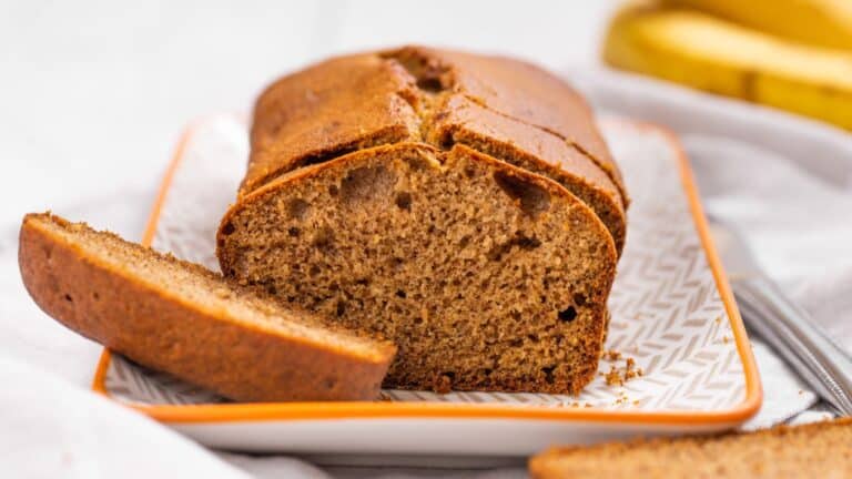 Sliced banana bread on a white patterned plate with a whole banana in the background.