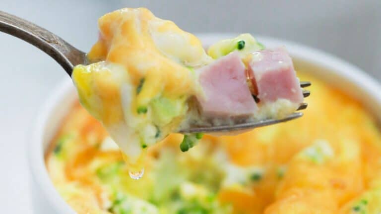 A fork holding a bite of mini frittata with ham and broccoli, with the dish in the background.