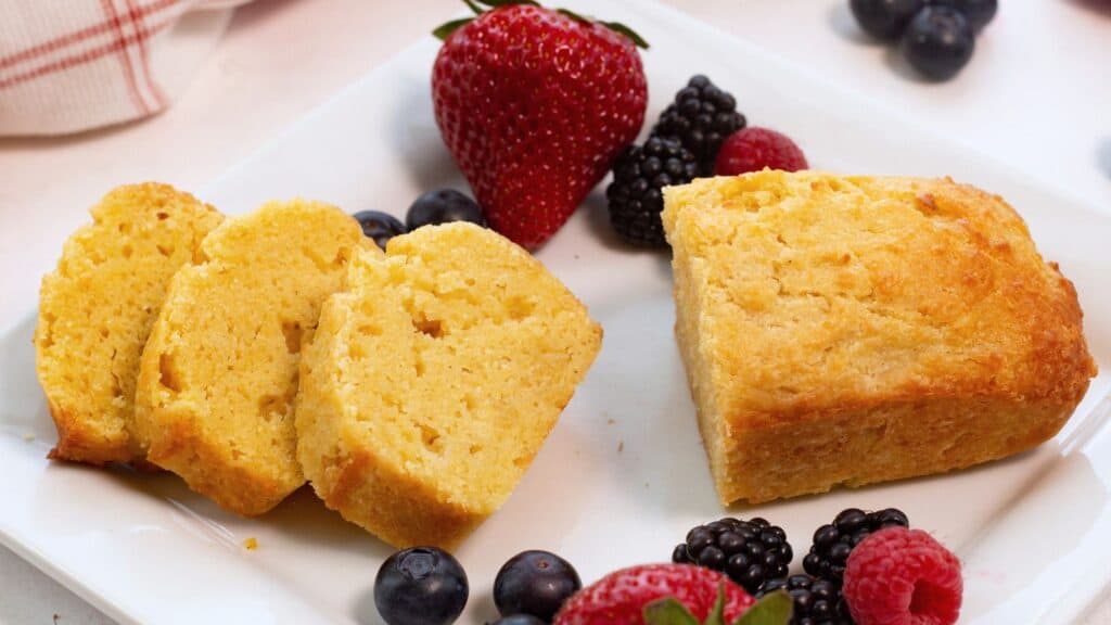 Mini pound cake loaf on square plate sliced with berries.