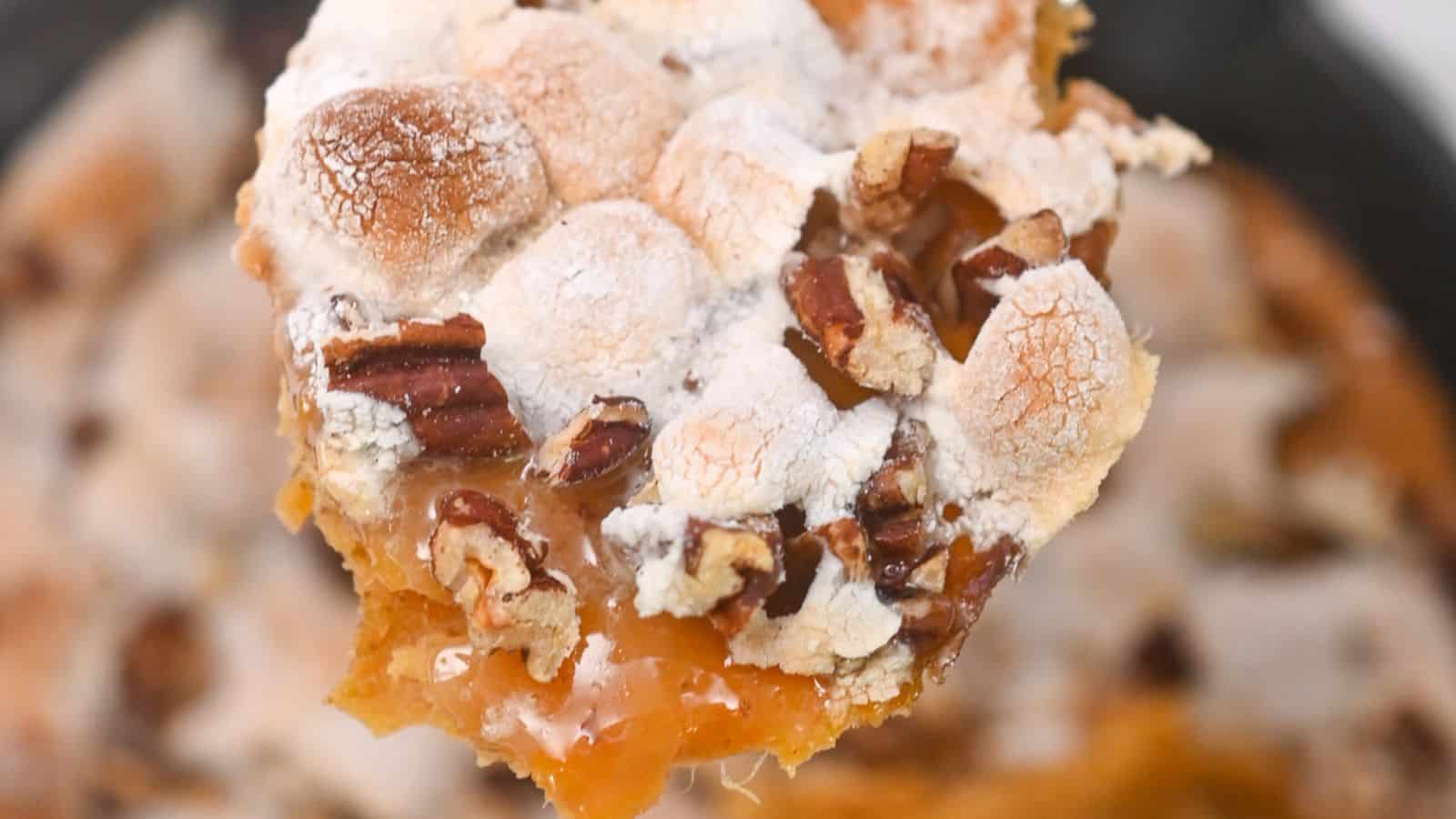 Close-up of a spoonful of sweet potato casserole with a topping of toasted pecans and marshmallows.