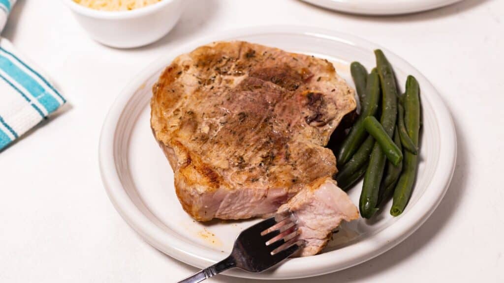 Oven baked pork steak on a plate with green beans and a fork on the side.