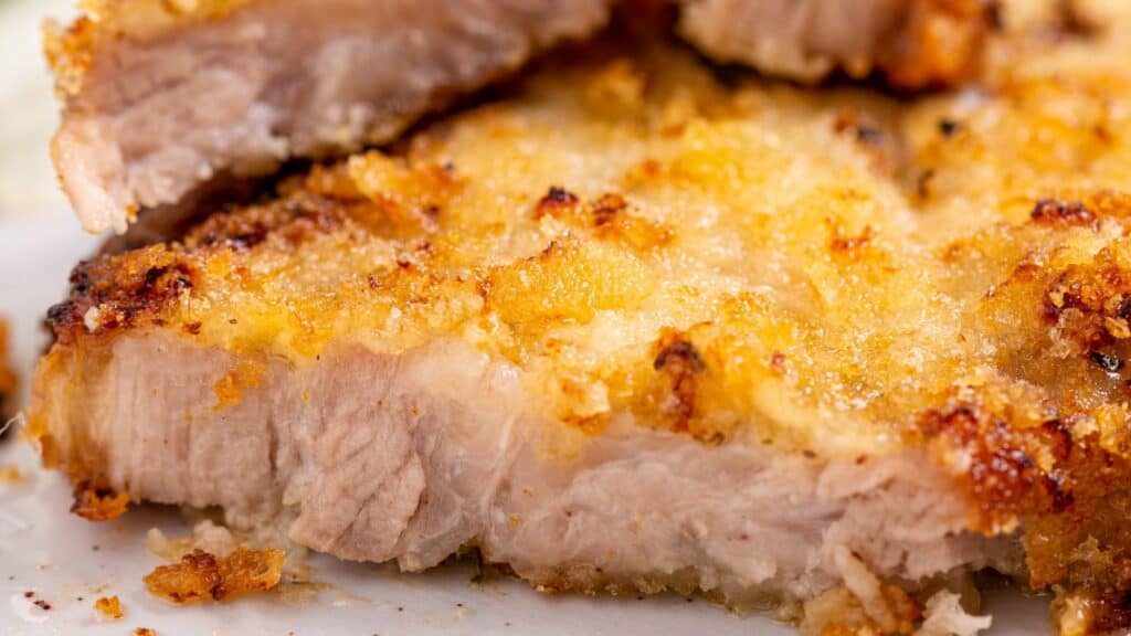 Close-up of a golden-brown crusted baked pork chop cut in half.