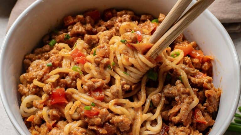 A bowl of noodles with meat sauce garnished with herbs.