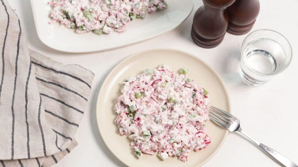 A plate of radish salad served on a table with a glass of water and salt and pepper shakers in the background.