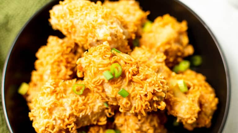 A bowl of fried chicken pieces coated with crispy instant noodle bits, garnished with chopped green onions.