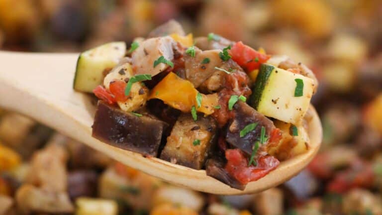 Close-up of a wooden spoon holding ratatouille, featuring chopped zucchini, bell peppers, and eggplant, garnished with parsley.