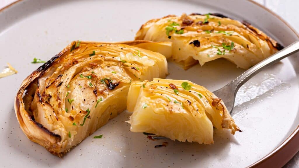 Sliced roasted cabbage steaks seasoned with herbs and spices on a white plate.