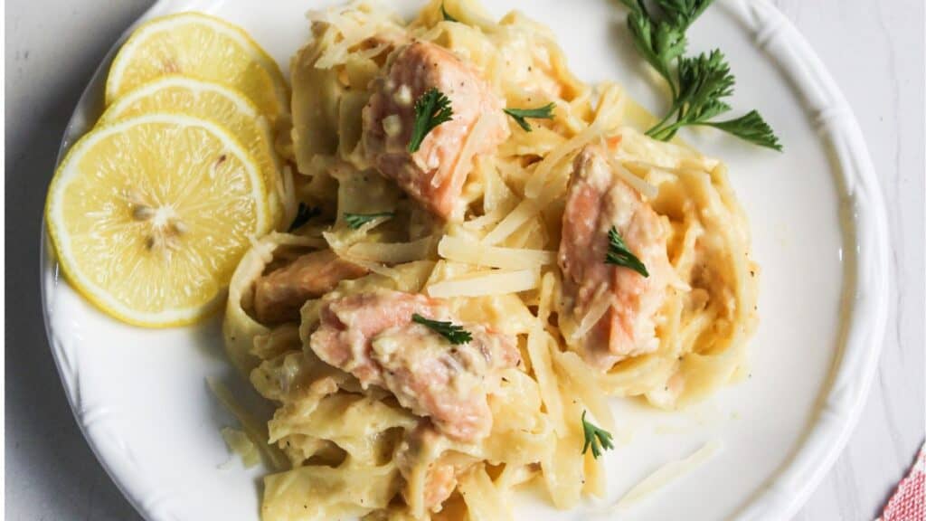 A plate of creamy salmon pasta garnished with lemon slices and parsley.