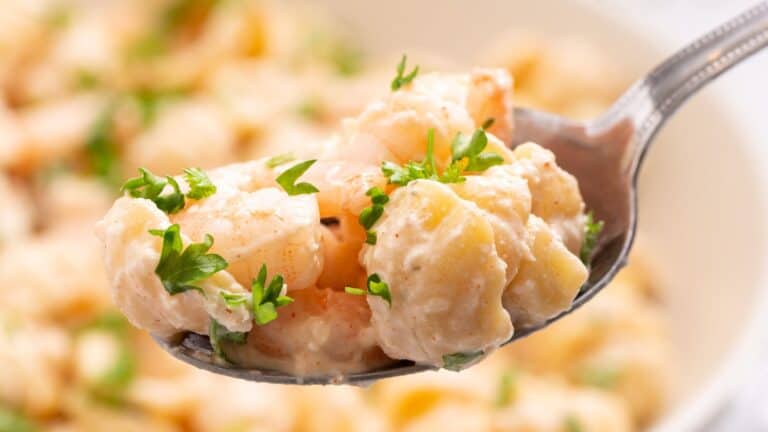 Close-up of a spoonful of shrimp salad with diced potatoes and garnished with fresh parsley, with more salad visible in the background.