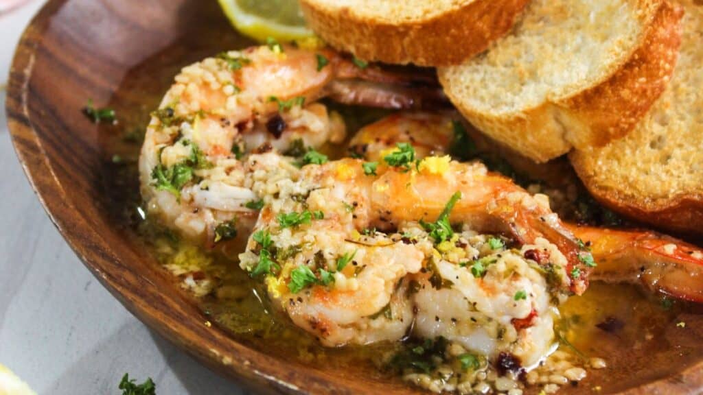 Seasoned shrimp served with slices of bread in a wooden bowl.