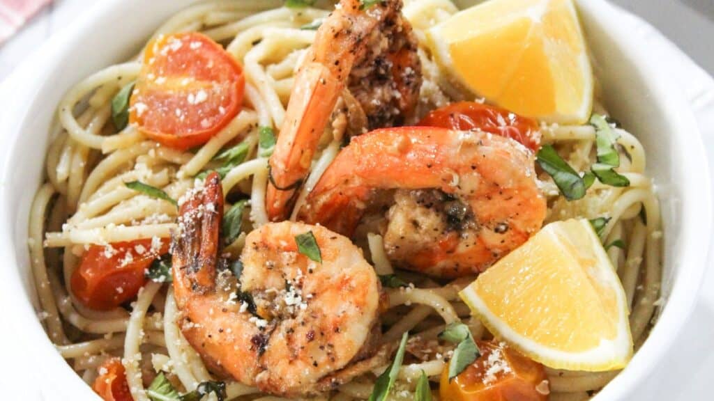 A bowl of shrimp pasta garnished with lemon wedges and fresh herbs.