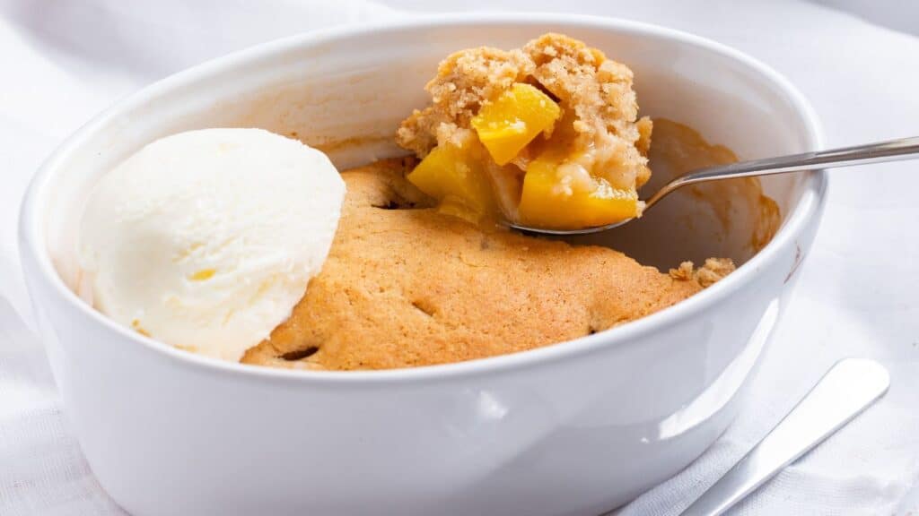 A serving of peach cobbler with a scoop of vanilla ice cream in a white bowl.