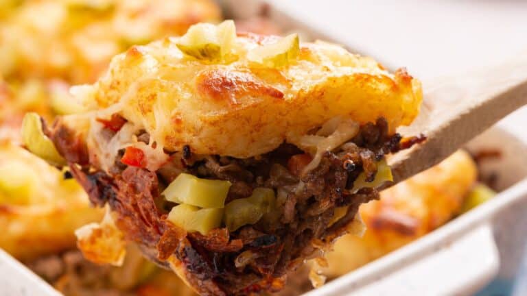 A close-up of a serving spoon lifting a portion of sloppy joe casserole showing layers of ground meat, vegetables, and golden-brown hashbrown potatoes.