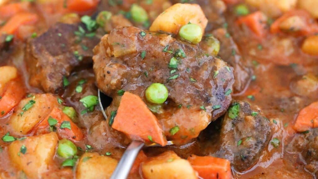 Hearty beef stew with carrots, peas, and potatoes, garnished with fresh herbs.