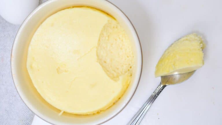 A serving of creamy yellow cheesecake with a spoon removing a piece, photographed from above on a white background.