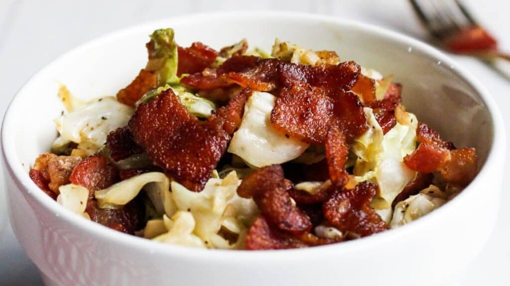 A bowl of sautéed cabbage topped with crispy bacon pieces.