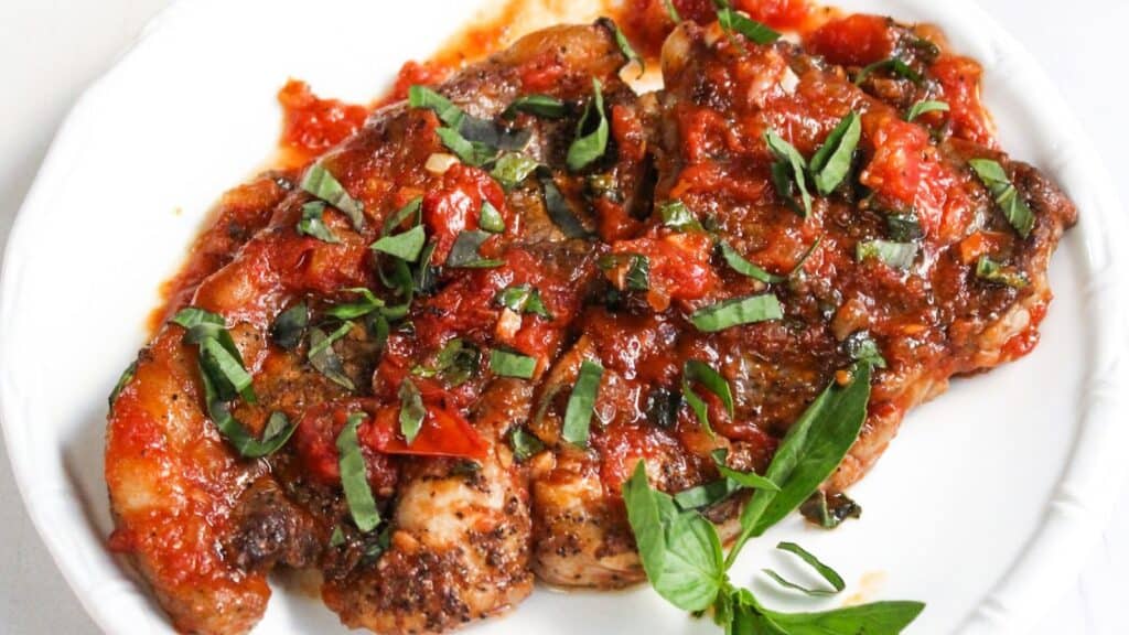 Fried steak topped with a chunky tomato and basil sauce, served on a white plate.