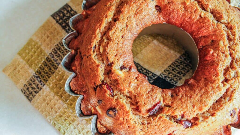 A bundt cake in a fluted pan rests on a checkered cloth.