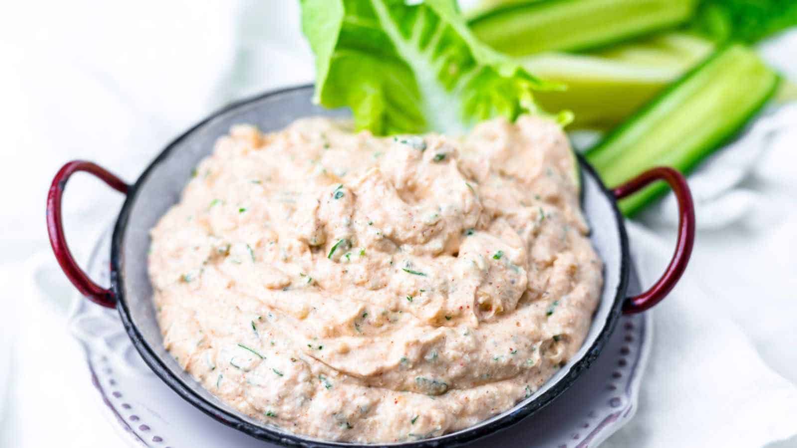 A bowl of Buffalo Ranch Sauce garnished with herbs, on a white cloth background.