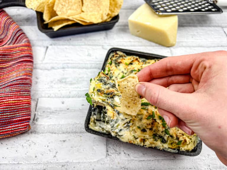 A hand dipping a tortilla chip into a tray of Copycat Applebee’s spinach artichoke dip.