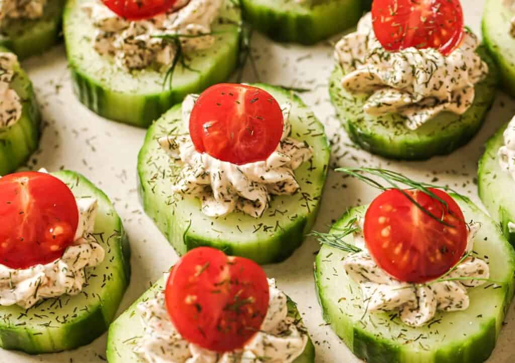 Slices of cucumber topped with a dollop of herbed cream cheese, a cherry tomato half, and a sprinkle of dill.