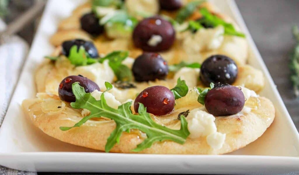 A plate of goat cheese flatbread served on a rectangular white dish.