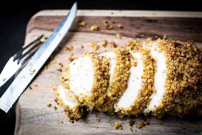 Sliced breaded chicken breast on a wooden cutting board with a knife next to it.