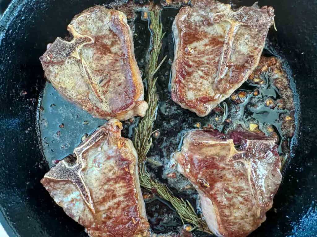 Lamb chops searing in a pan with rosemary, close-up view.