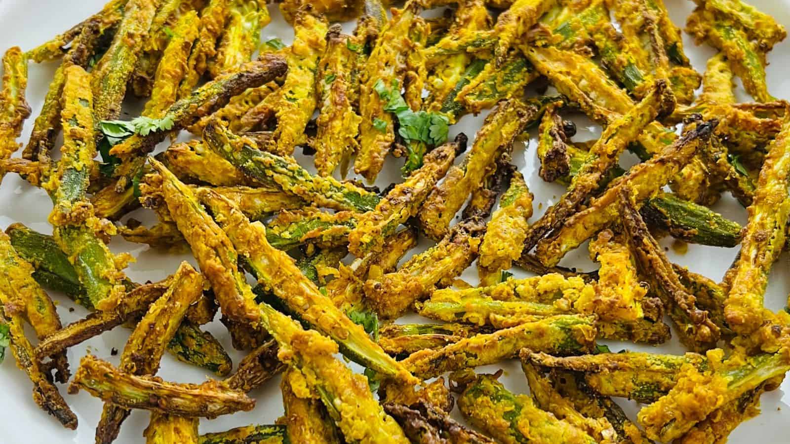 A plate of crispy, golden-fried okra seasoned with spices and garnished with a few cilantro leaves.